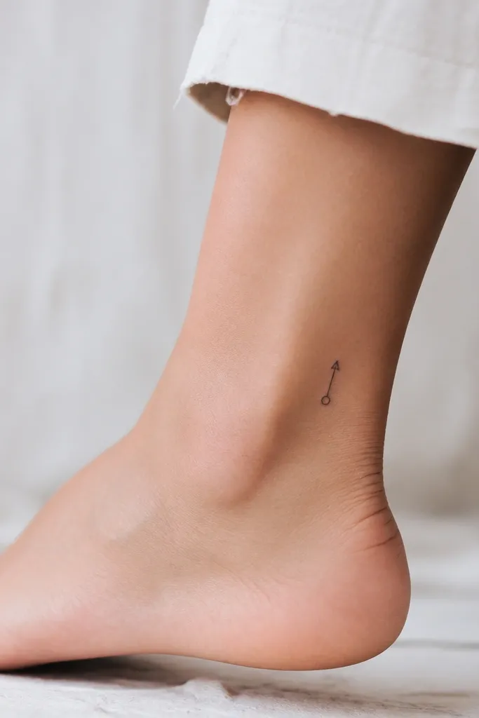 A tiny compass needle with a simple arrow tip and a small circle, black ink, on the outer ankle.