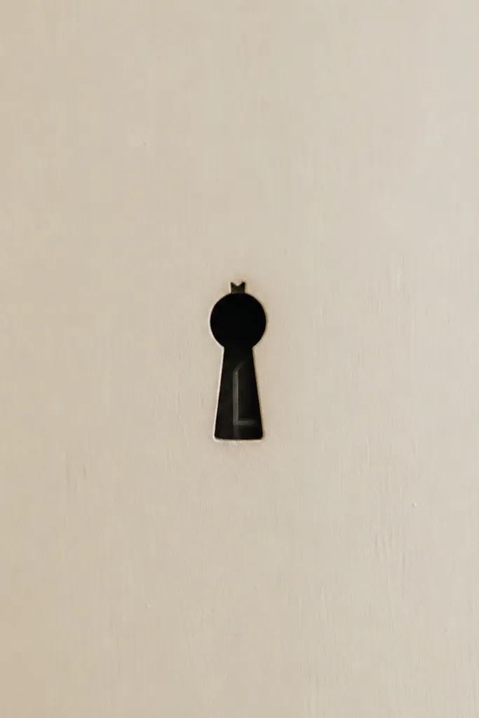 A tiny keyhole silhouette in black with a small crown-like notch at the top. Inside, there is a single thin line that suggests a doorway or ward.