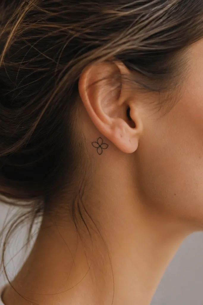 A tiny three-petal flower bud behind the ear, black ink with a small dot center, no heavy shading.