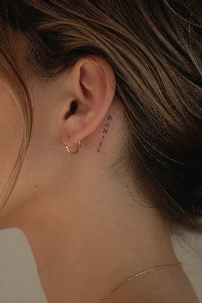 Behind the ear: the boyfriend's name in very small black serif letters, stacked or slightly arched, with no extra icons. The letters are clean and evenly spaced.
