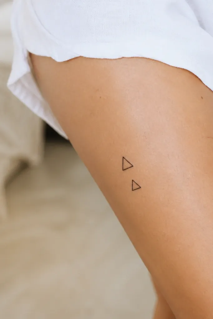 Two small black outline triangles stacked diagonally on the outer thigh above the knee, one slightly larger than the other.