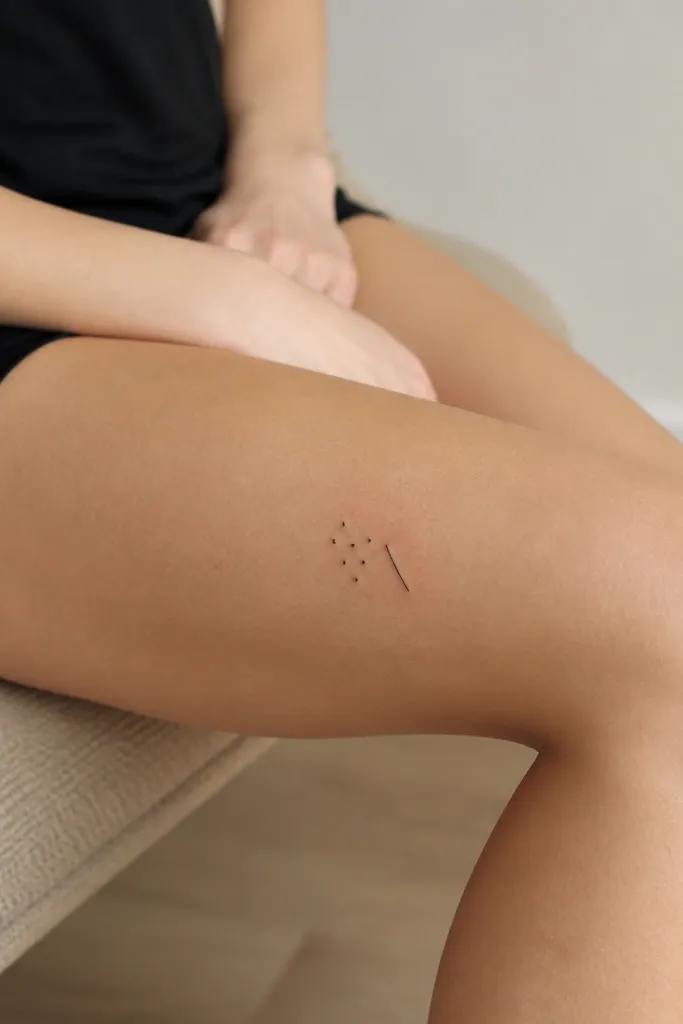 A small cluster of 6-8 tiny black dots with one short black line segment beside them on the outer thigh above the knee.