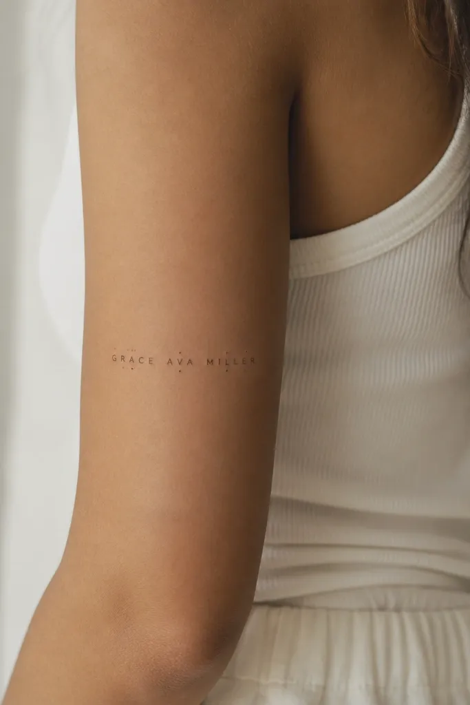 A name written horizontally across the back of the upper arm in fine print, with tiny dot separators above and below certain letter clusters. The dots are very small and spaced evenly.