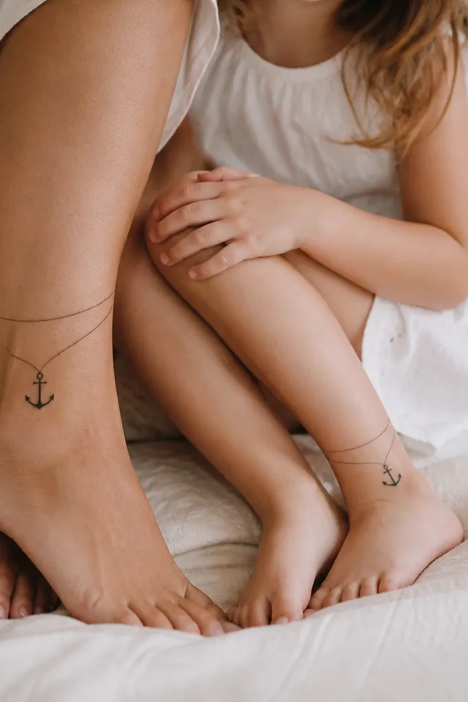 A small black anchor outline on mom's ankle with two thin rope lines wrapping upward. Daughter has a matching anchor on her inner ankle with the ropes drawn slightly thinner.