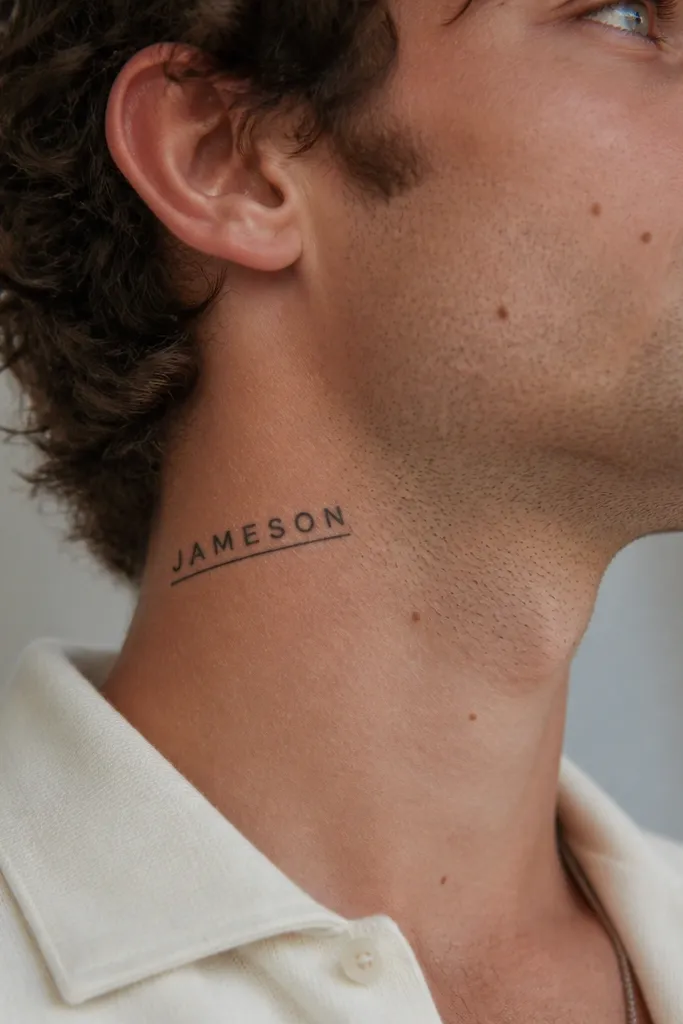 A small-caps name tattoo on the side of the throat, angled slightly upward. A single thin line runs under the name like a bookmark. Solid black letters with sharp corners.