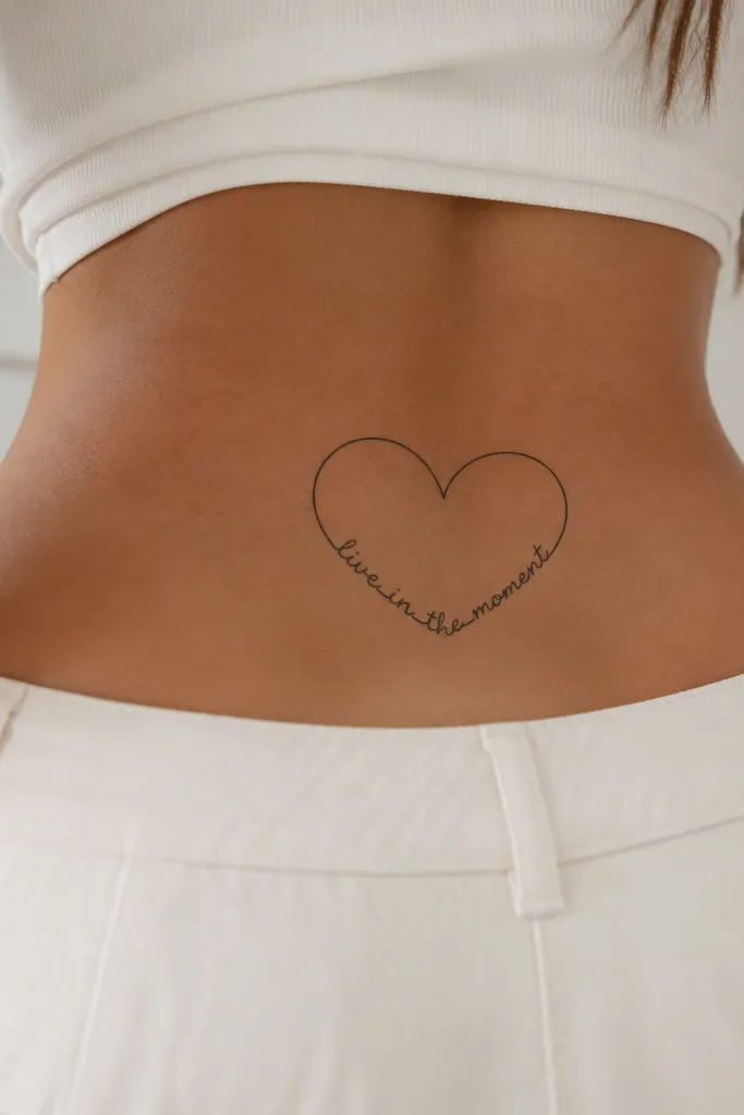 A thin black heart outline on the lower back, with a short phrase written inside the heart, centered, no fill, letters aligned to the heart curve.