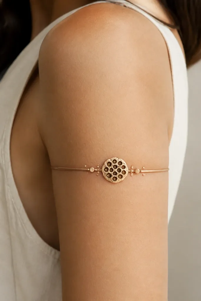 A narrow band wraps the upper arm with a lotus seed pod shape centered, plus small dot highlights around it like pollen.